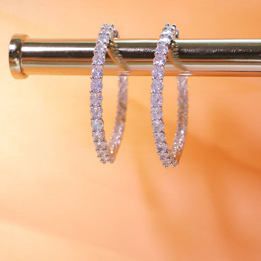 Diamond hoop earrings on a metallic stand with a blurred orange background