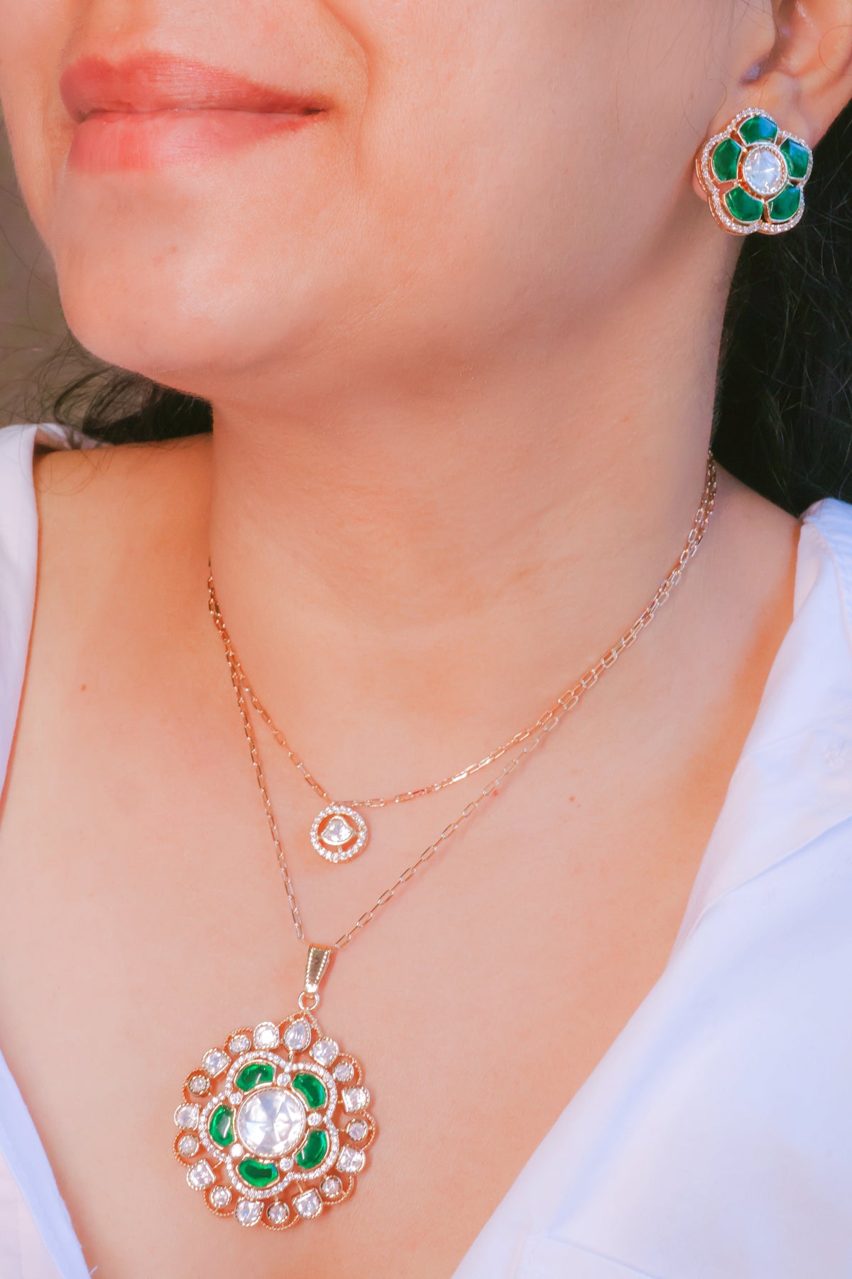 Rose gold necklace and earrings with green gemstones on a person wearing a white top.