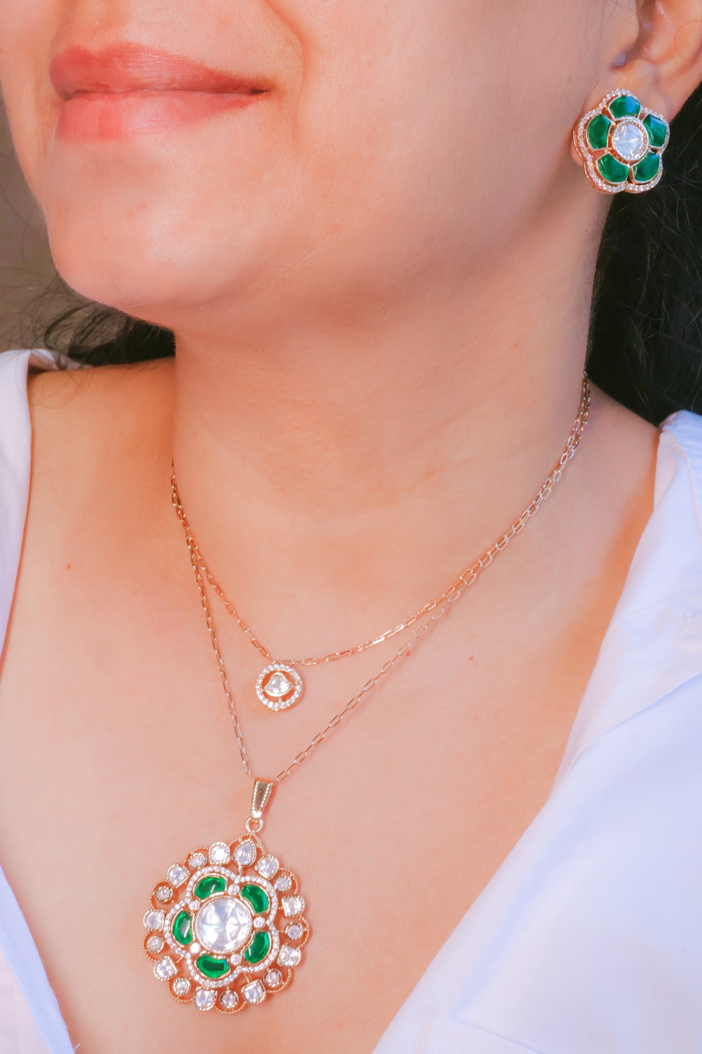 Rose gold necklace and earrings with green gemstones on a person wearing a white top.