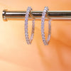 Diamond hoop earrings on a metallic stand with a blurred orange background